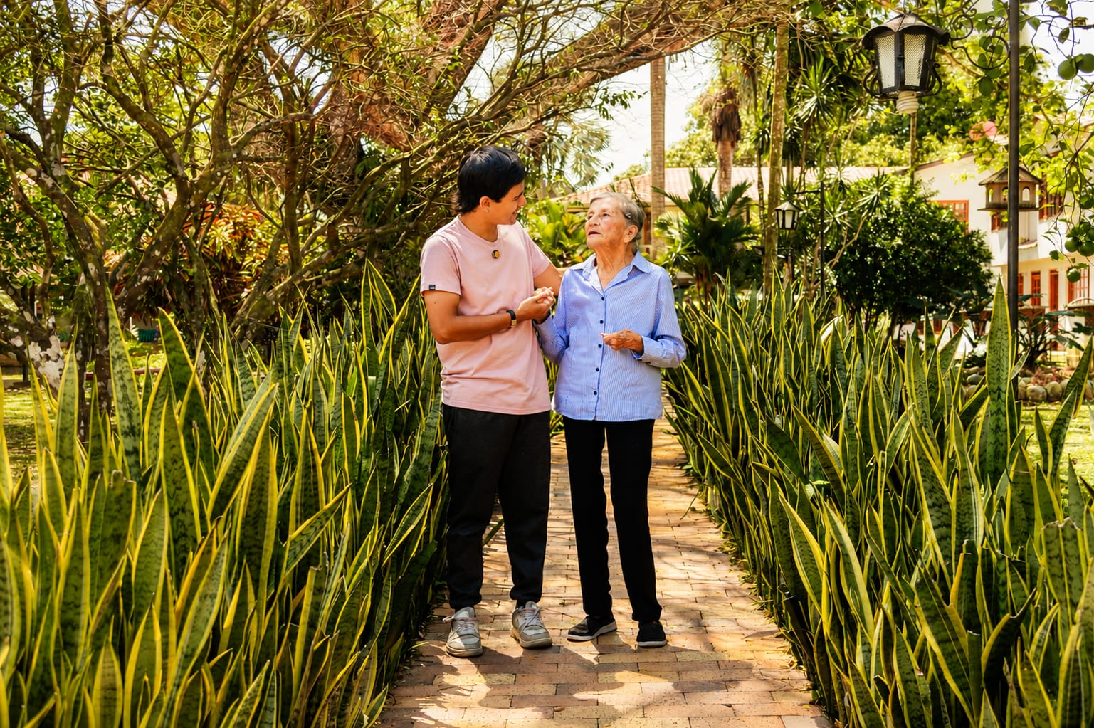 Acompañante caminando junto a una residente en los jardines de Talentos con Amor